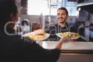 Smiling young waiter giving food to waitress at counter