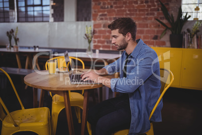 Side view of handsome man typing on laptop while sitting at table