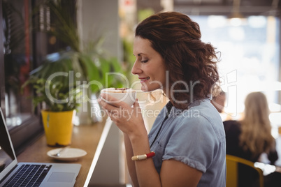 Young woman smelling coffee while sitting at cafe