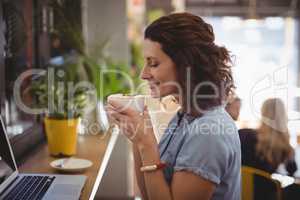 Young woman smelling coffee while sitting at cafe