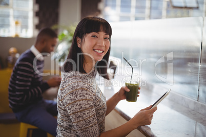 Portrait of smiling young woman holding drink and tablet