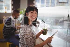 Portrait of smiling young woman holding drink and tablet