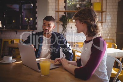 Young man gesturing at laptop while sitting by woman