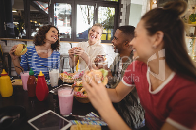 Cheerful young friends sitting with food and drink at table