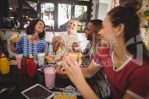 Cheerful young friends sitting with food and drink at table