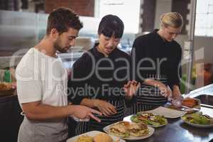 Female chef talking with waiter by colleague at kitchen