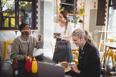 Young man ordering food to waitress while sitting with female friend