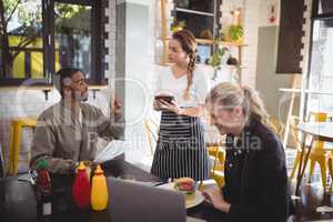 Young man ordering food to waitress while sitting with female friend