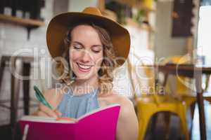 Smiling beautiful young woman writing in pink dairy
