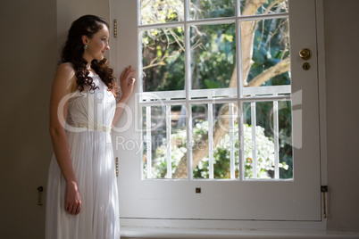 Smiling bride looking through window while standing at home