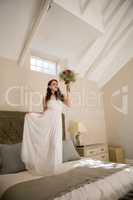 Beautiful bride holding bouquet while standing on bed