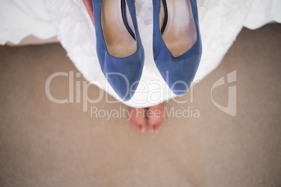 Low section of bride holding blue shoes while sitting in fitting room
