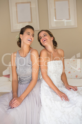 Happy bride with bridesmaid sitting on bed