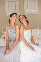 Happy bride with bridesmaid sitting on bed