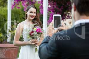Bridegroom photographing bride holding bouquet at park