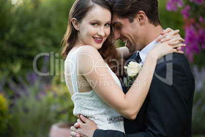 Happy bride embracing bridegroom while standing in park