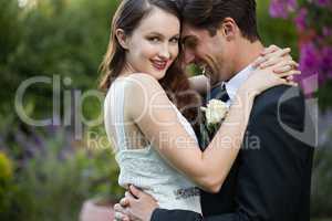 Happy bride embracing bridegroom while standing in park