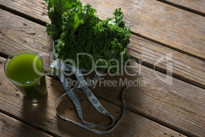 Mustard greens, measuring tape and juice on wooden table