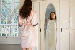 Bride trying on dress while standing by mirror at home