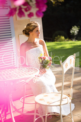 Beautiful bride holding bouquet while sitting on chair in yard