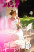 Beautiful bride holding bouquet while sitting on chair in yard