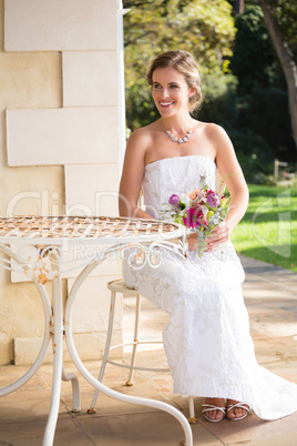 Beautiful bride with bouquet looking away while sitting in yard