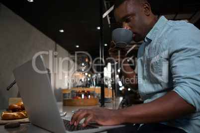 Man drinking coffee while using laptop at counter