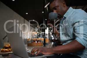 Man drinking coffee while using laptop at counter
