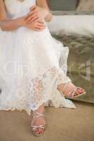 Low section of bride wearing silver sandals sitting on bed