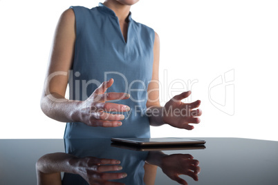 Mid section of businesswoman gesturing over digital tablet at table