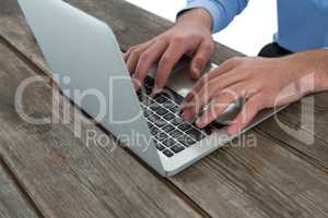 Cropped image of businessman using laptop at wooden table