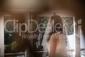 Beautiful bride in wedding dress looking through window