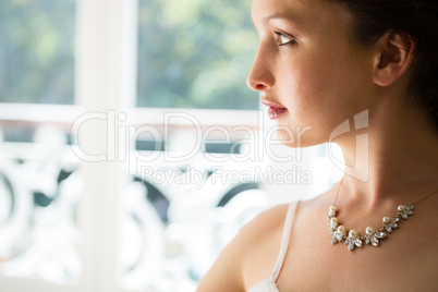 Beautiful bride wearing necklace looking through window at home