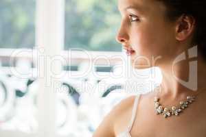 Beautiful bride wearing necklace looking through window at home