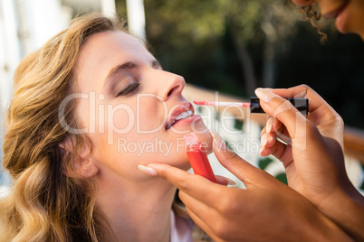 Cropped hand of beautician applying lip gloss to bride
