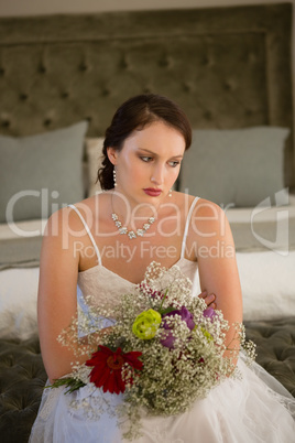 Sad bride with bouquet sitting on bed