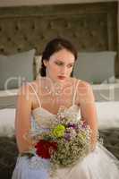 Sad bride with bouquet sitting on bed