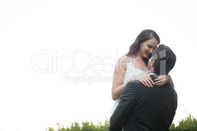 Bridegroom lifting bride while standing against clear sky in park