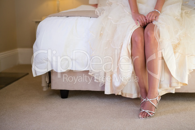 Low section of bride wearing sandals sitting on bed