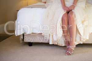 Low section of bride wearing sandals sitting on bed