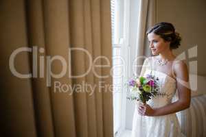 Bride with bouquet looking through window at home