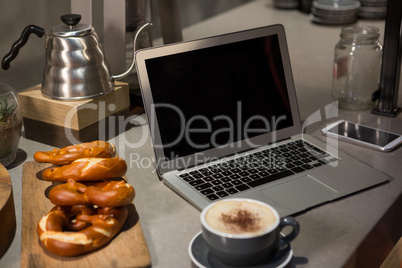 Close-up of coffee, laptop and pretzel at counter