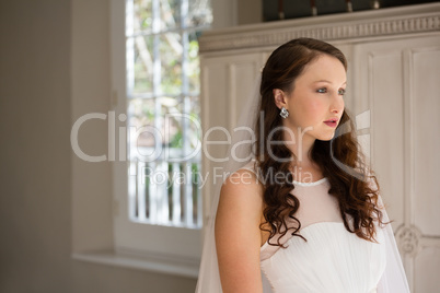 Thoughtful bride looking away while standing at home