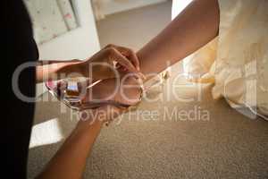 Cropped hands of beautician putting on sandal to bride at home