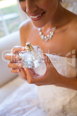Midsection of smiling bride holding perfume sprayer while sitting on armchair
