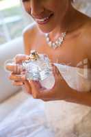 Midsection of smiling bride holding perfume sprayer while sitting on armchair