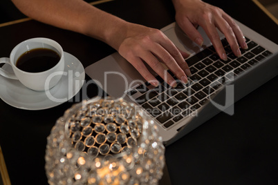 Close-up of woman using laptop while having coffee