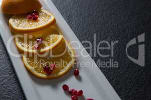 Slice of orange with pomegranate seeds in tray