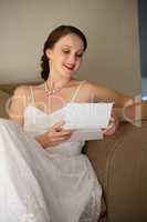 Happy bride reading wedding card while sitting on sofa