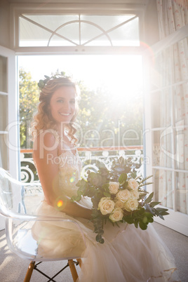 Portrait of happy bride holding bouquet while sitting on chair